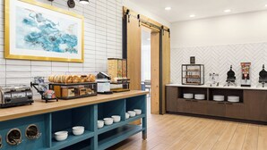 A breakfast bar with a coffee machine, toaster, and bread display, a framed abstract painting, and a herringbone-patterned wall. - Staybridge Suites Detroit Woodhaven by IHG (Woodhaven)