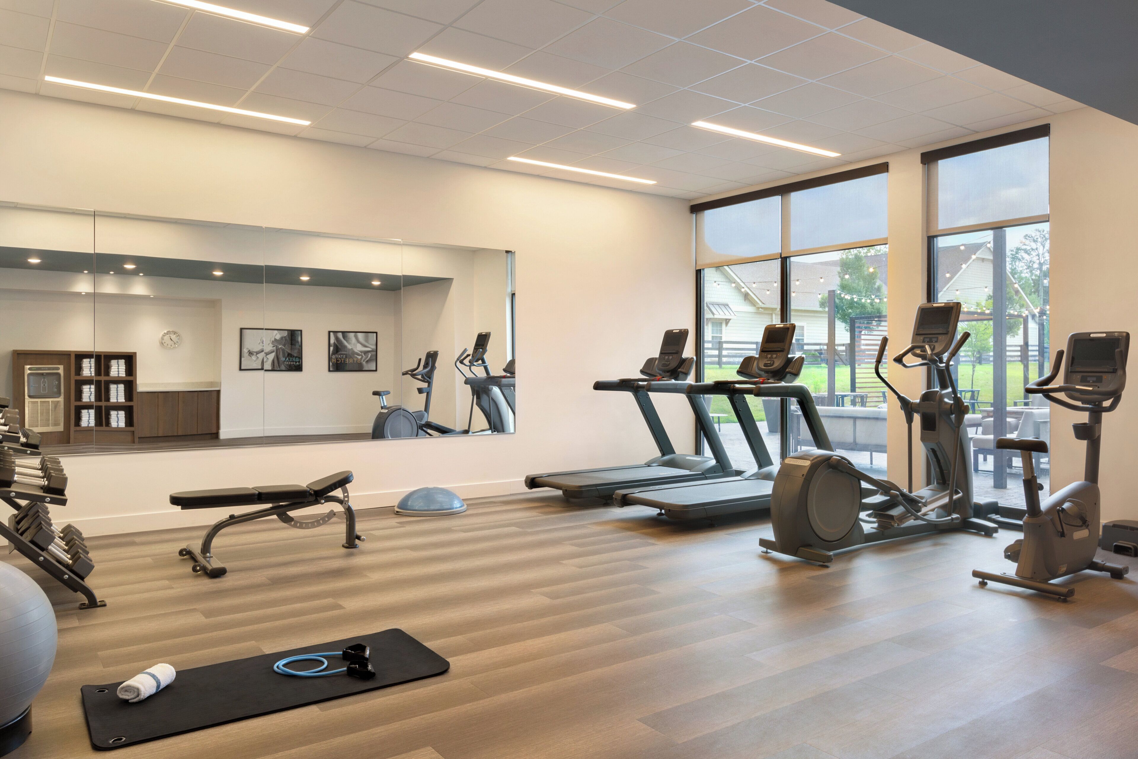 A gym with exercise equipment, a mirror, and large windows.