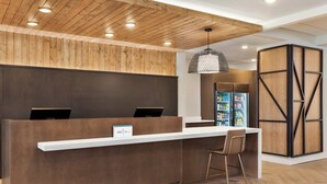 A reception desk with a wooden panel wall, a white counter, and a hanging pendant light. - Staybridge Suites Detroit Woodhaven by IHG (Woodhaven)