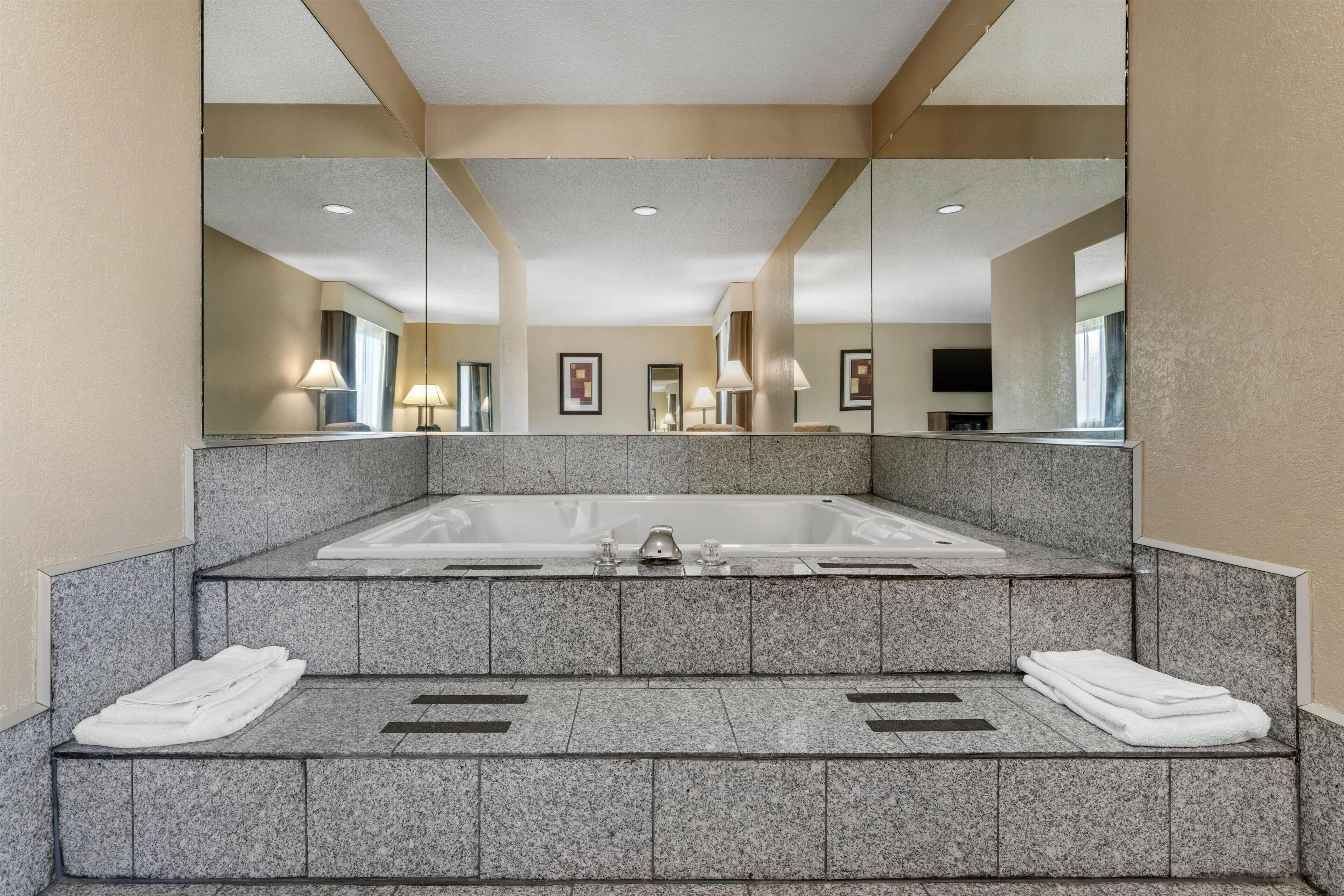 Une grande baignoire rectangulaire dotée d’une zone de douche, d’un miroir et de deux serviettes posées sur les marches.