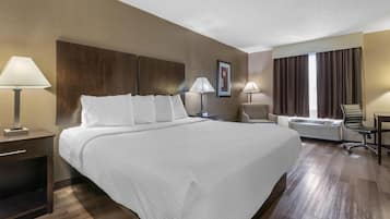 Een hotelkamer met een groot bed, nachtlampen, een bureau, een bureaustoel, een raam met gordijnen en een airconditioning.