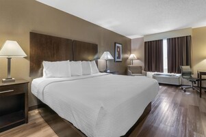 Habitación de hotel con una cama grande, lámparas de noche, un escritorio, una silla de oficina, una ventana con cortinas y un equipo de aire acondicionado.