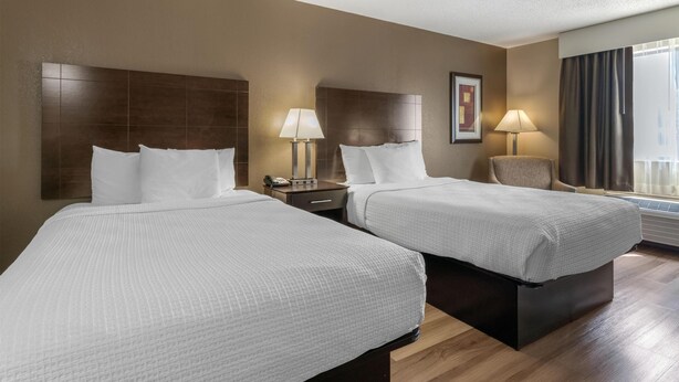 A hotel room with two beds, a nightstand, a chair, a lamp, and a framed picture on the wall. - Best Western Muncie (Muncie)