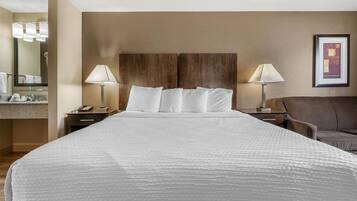 Habitación de hotel con una cama grande, dos lámparas de noche, un cabecero de madera, un baño con espejo y un cuadro en la pared.