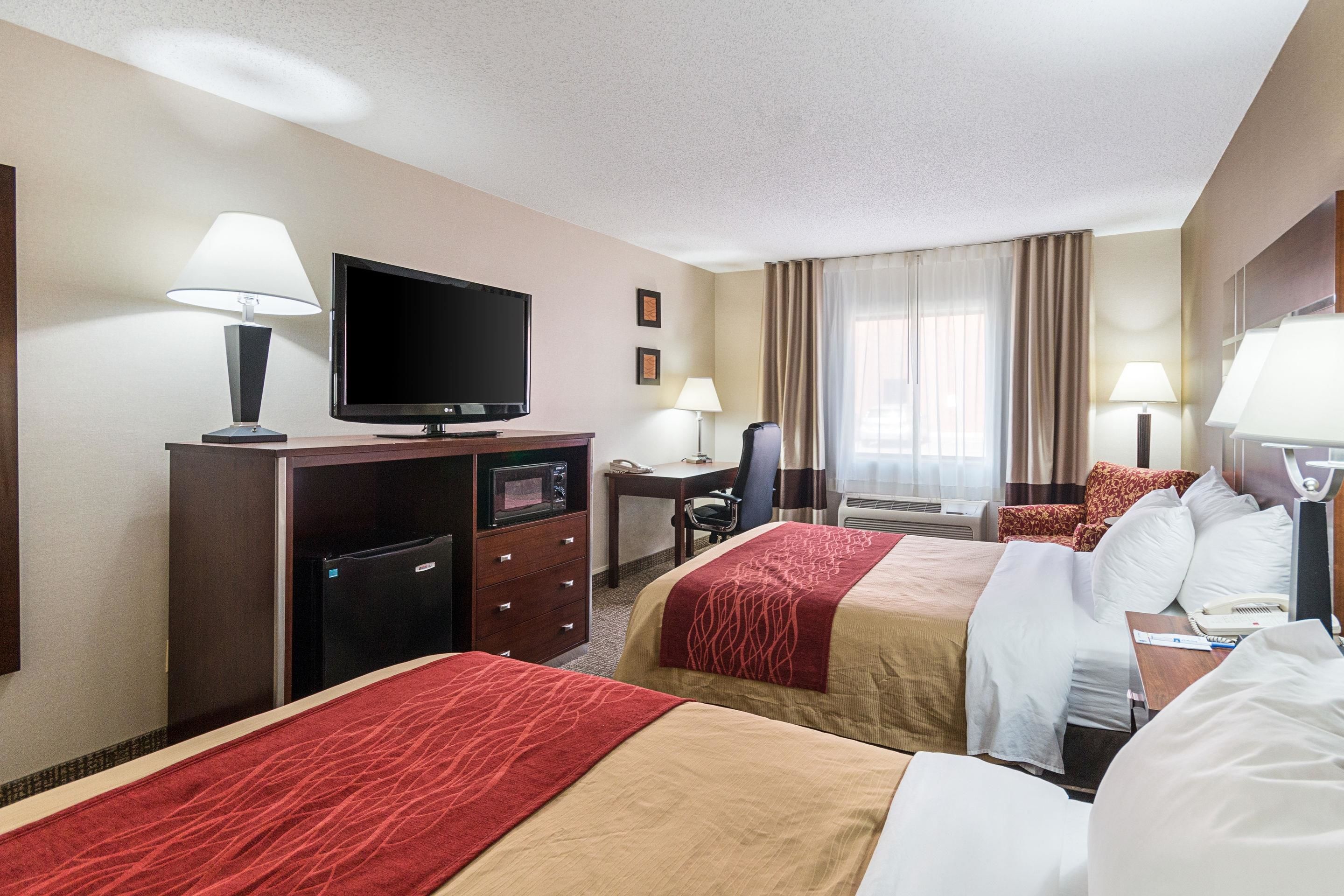 A hotel room with two beds, a desk, a television, and a minibar.