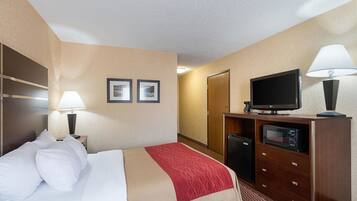 A hotel room with a bed, a desk with a lamp, a television, and a minibar.