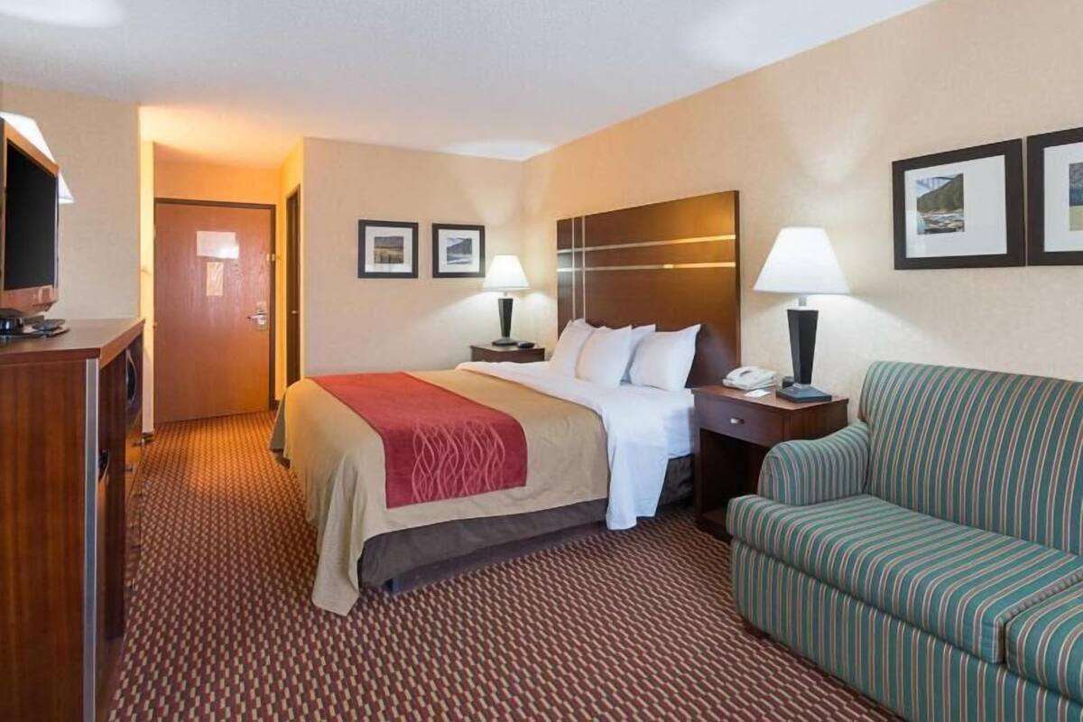 A hotel room with a bed, a desk, a chair, and a television.