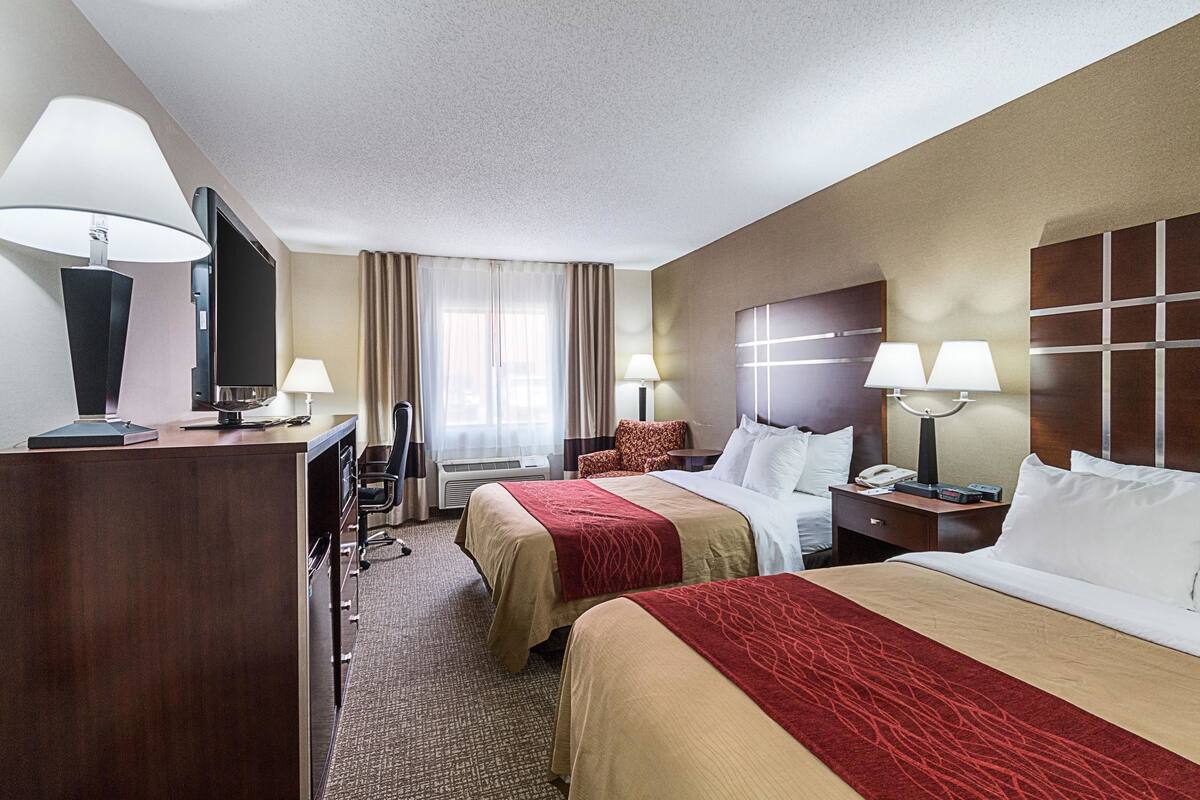 A hotel room with two beds, a desk, a TV, and a window with curtains.