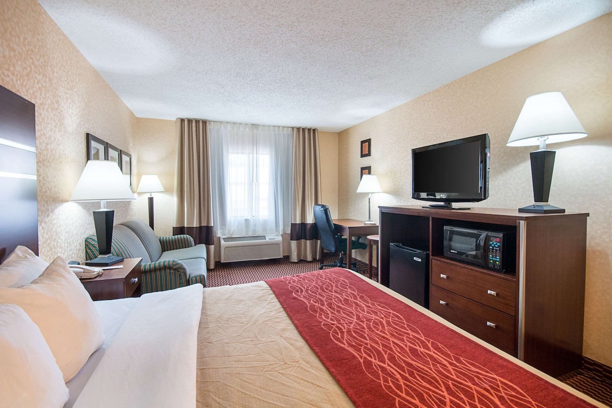 A hotel room with a bed, a desk, a television, a microwave, and a window with curtains.