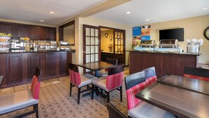 A hotel dining area with a buffet, wooden furniture, and a television on the wall. - Quality Inn Parkersburg North - Vienna (Parkersburg)