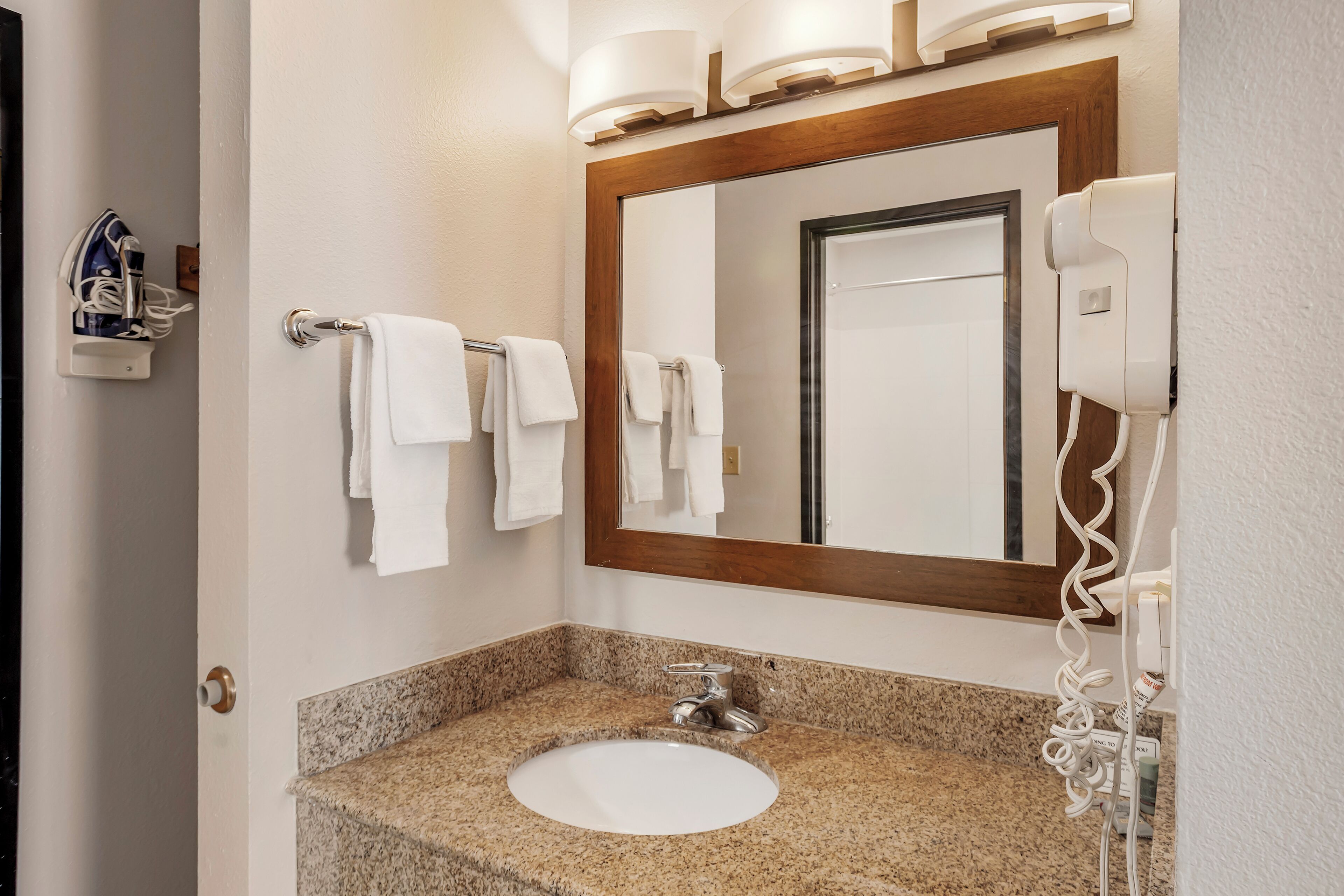 A bathroom with a granite countertop sink, a large mirror, and a hairdryer mounted on the wall.