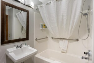 Un baño con lavamanos blanco, espejo y bañera. Hay una cortina de ducha y un perchero.