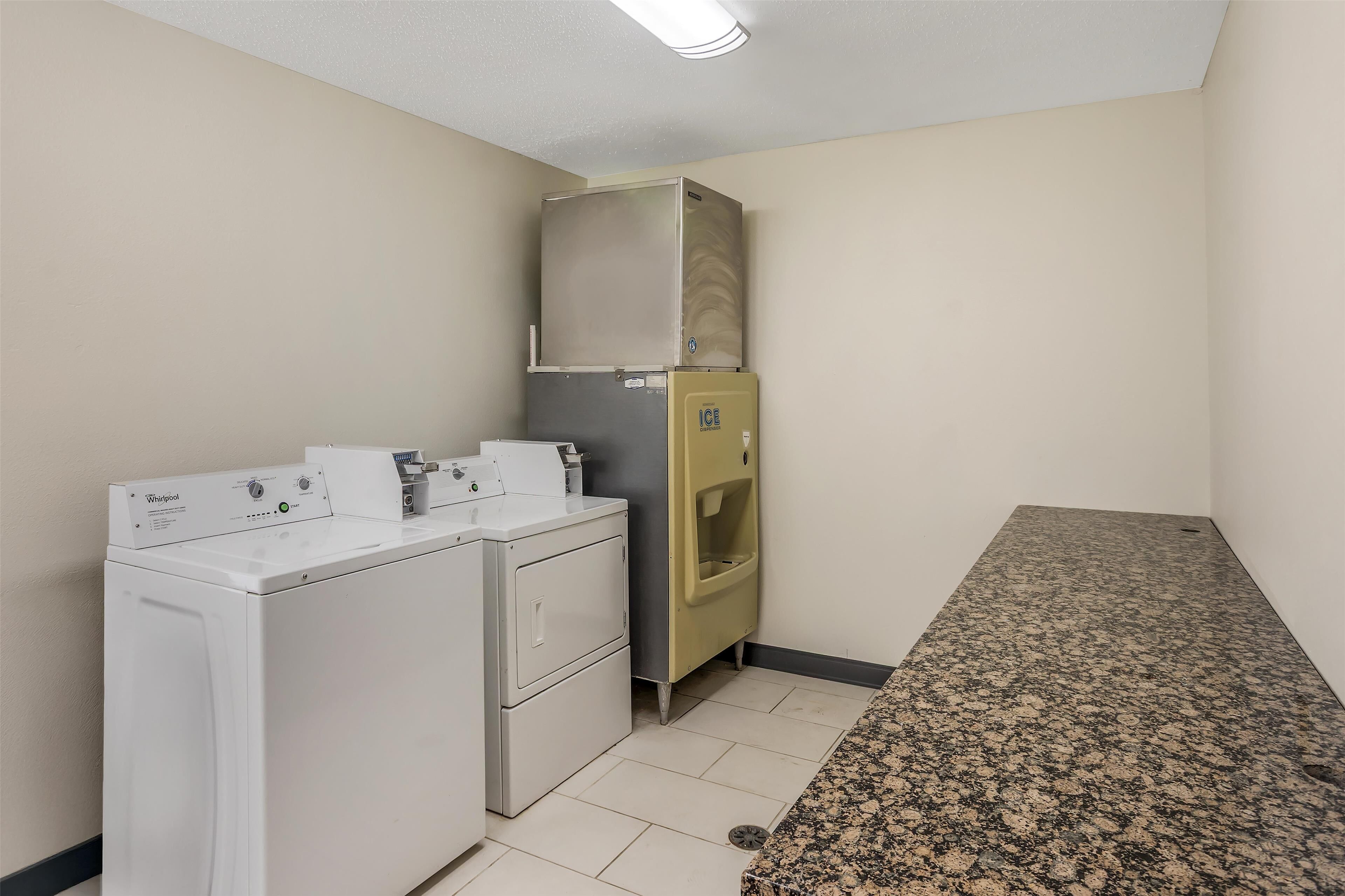 Un cuarto de lavandería con lavadora y secadora Whirlpool, un refrigerador pequeño y una encimera de granito.