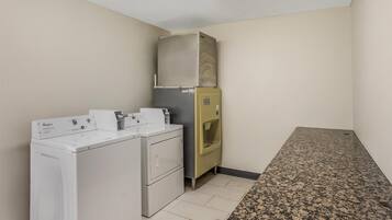 Un cuarto de lavandería con lavadora y secadora Whirlpool, un refrigerador pequeño y una encimera de granito.