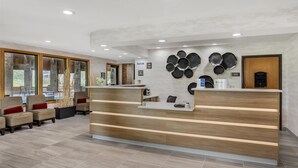 Un área de recepción moderna con un mostrador de madera, zona de estar con sillas acolchadas y una pared decorada con placas metálicas circulares.