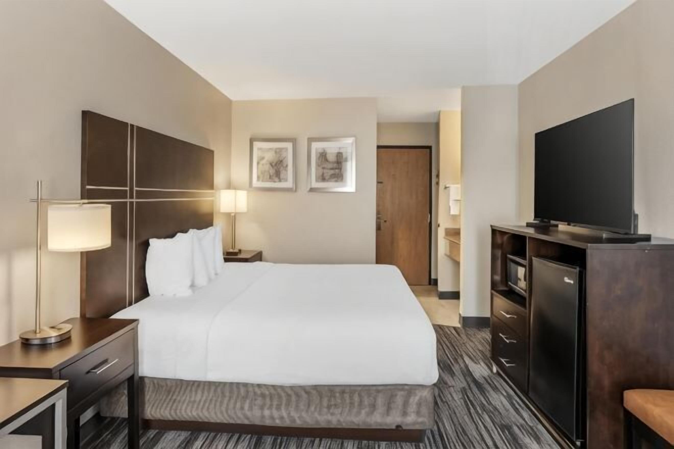 Ein Hotelzimmer mit einem großen Bett, einem Fernseher, einem Schreibtisch mit Lampe und einem Kleiderschrank.