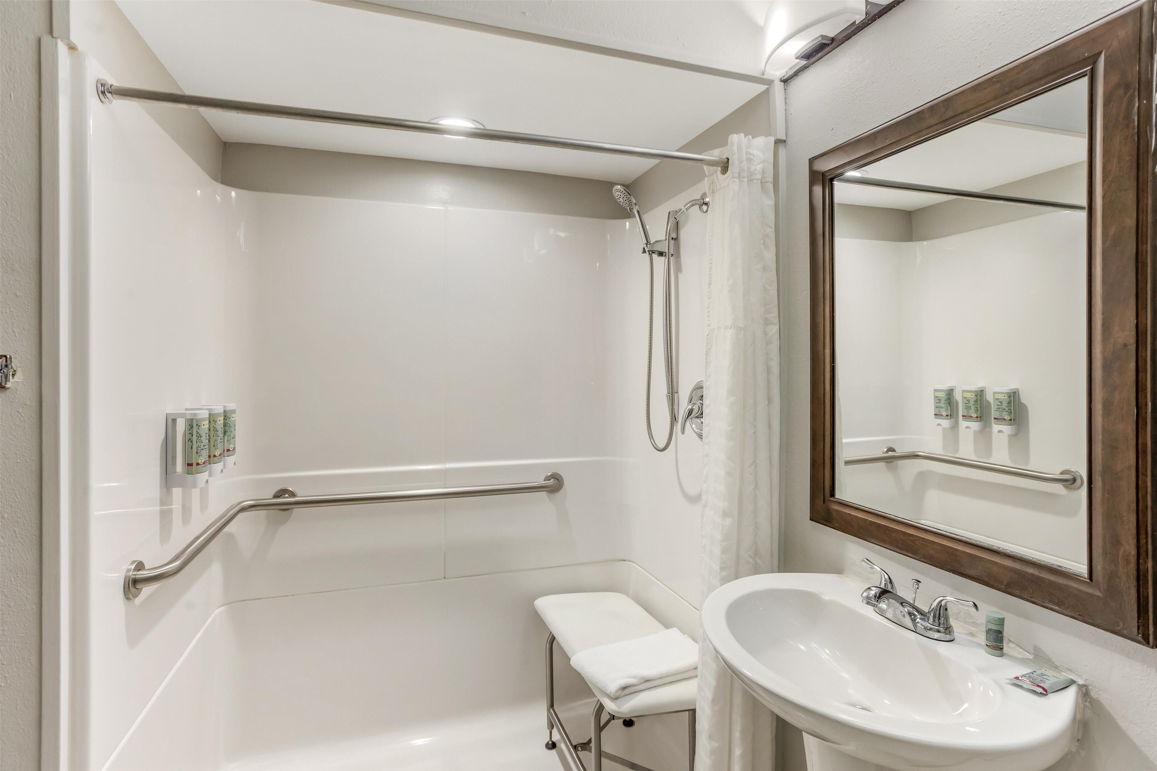 A bathroom with a white sink, a mirror, a shower with a handheld showerhead, and a grab bar.