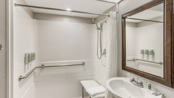 A bathroom with a white sink, a mirror, a shower with a handheld showerhead, and a grab bar.