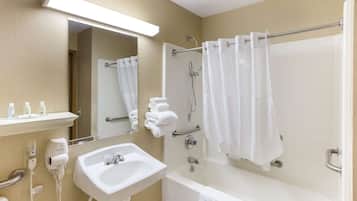 A bathroom with a sink, mirror, towel rack, shower, and a towel dispenser.