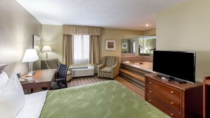 A hotel room with a bed, a desk with a lamp, a chair, a television, and a bathroom with a bathtub and mirror. - Quality Inn Athens (Athens)