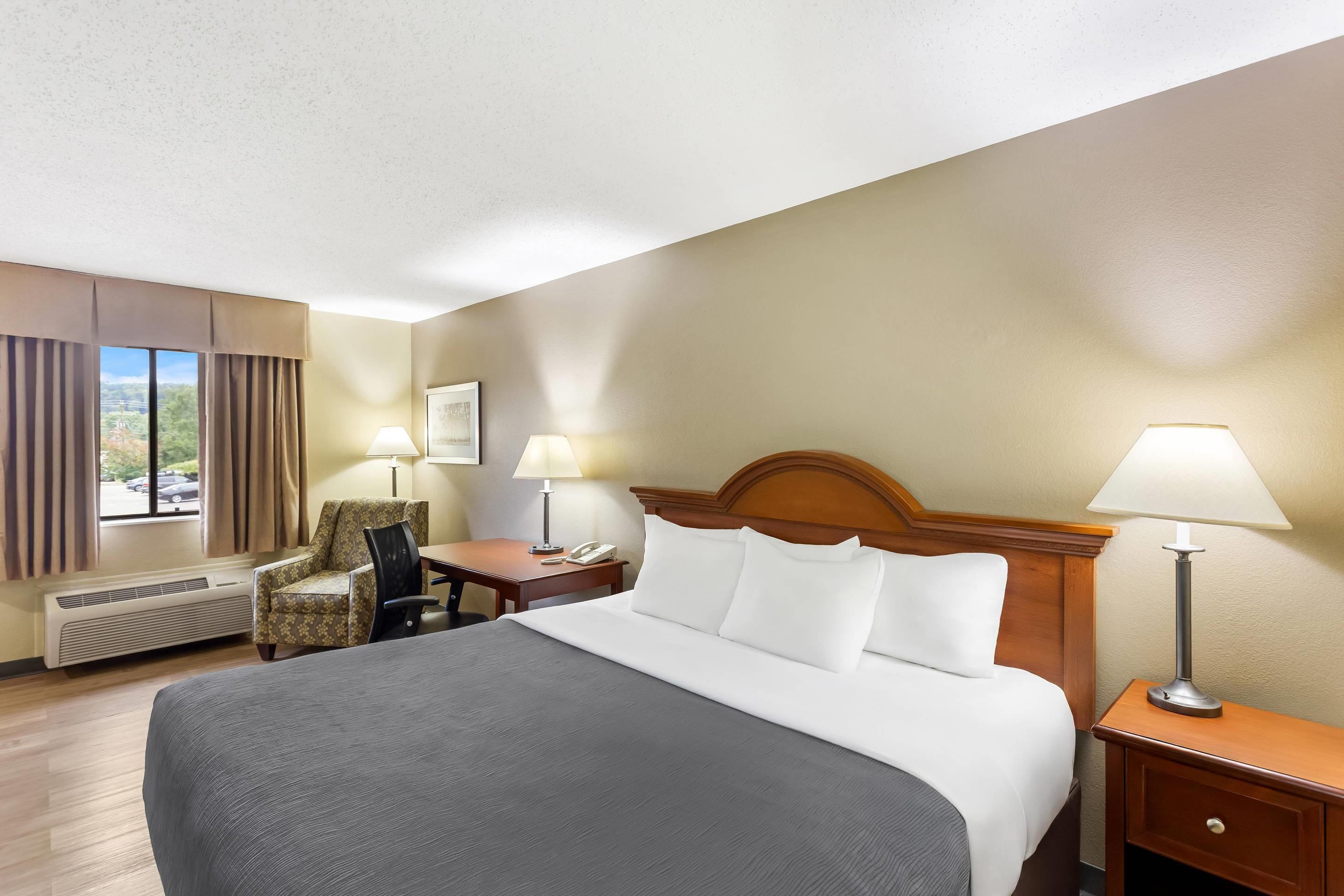 A hotel room with a bed, two bedside lamps, a chair, a desk with a phone, and a window with curtains.