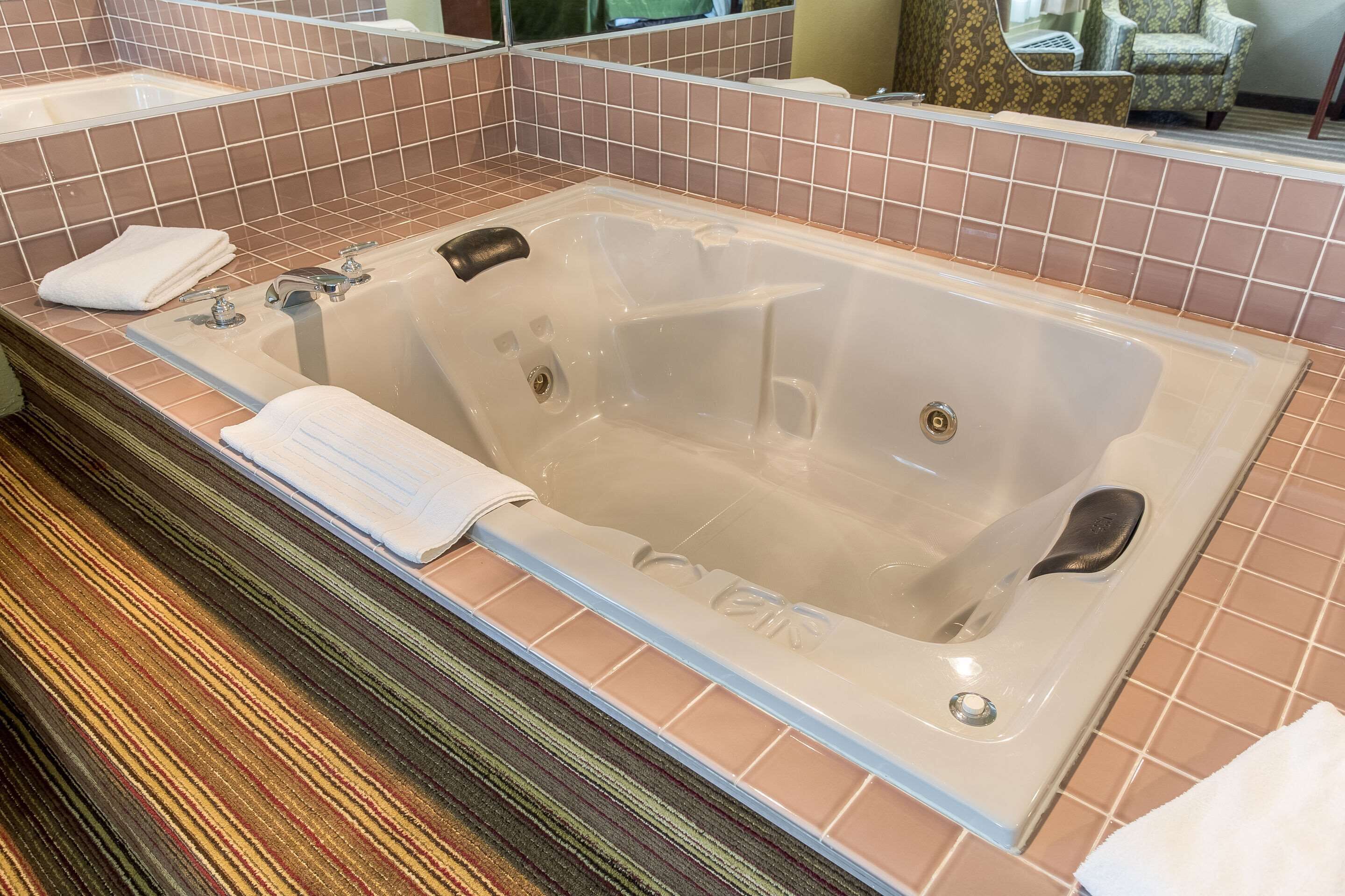 A large, clear bathtub with a single faucet and a control panel, surrounded by a tiled wall and a wooden floor.
