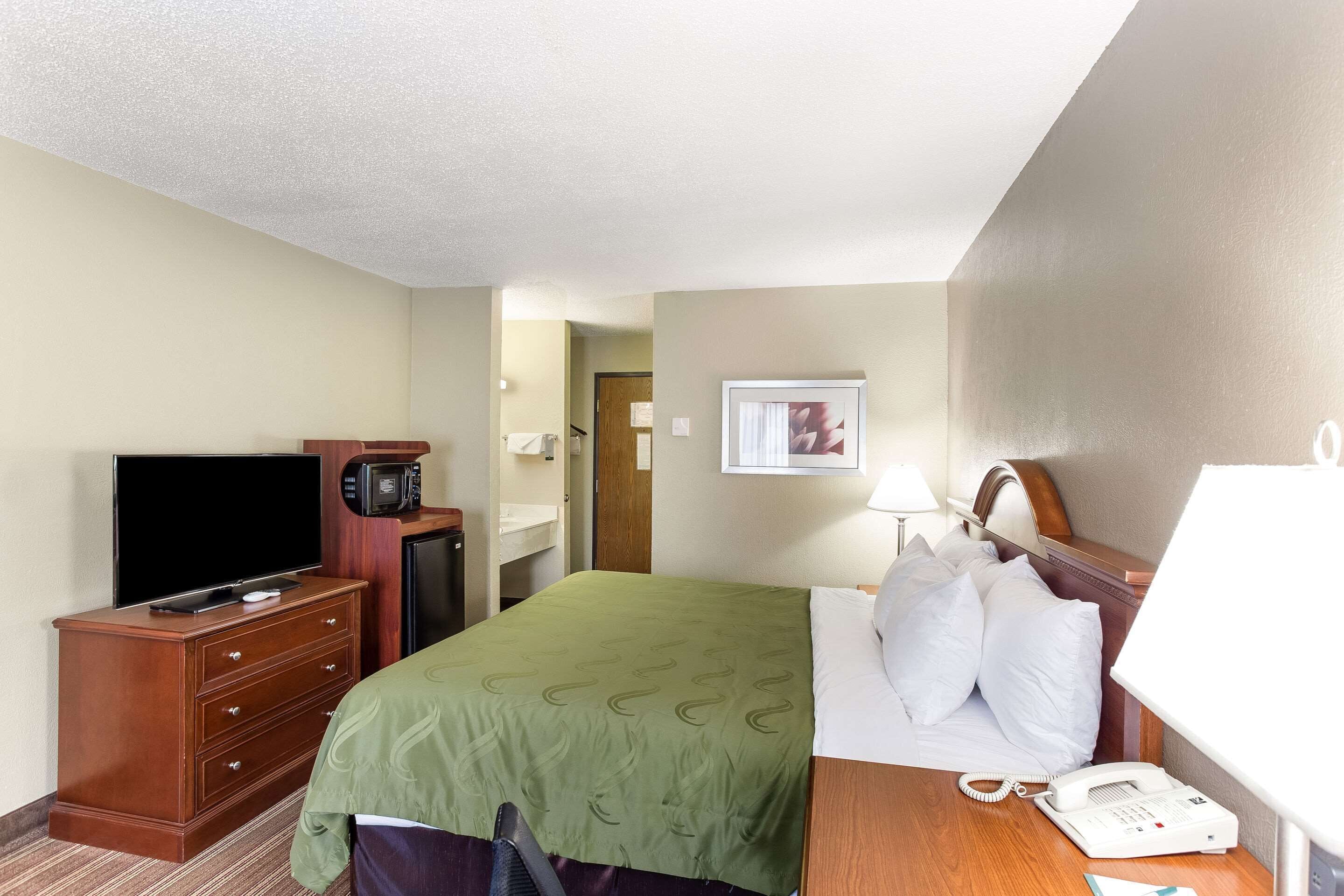 Una habitación de hotel con una cama, un escritorio con teléfono, televisor y microondas.