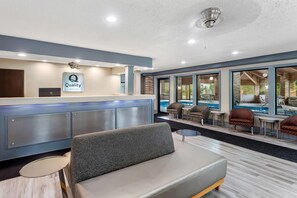 A hotel reception area with a sign for 'Quality by Choice Hotels,' a reception desk, a seating area with a sofa and chairs, and a view of an outdoor pool.
