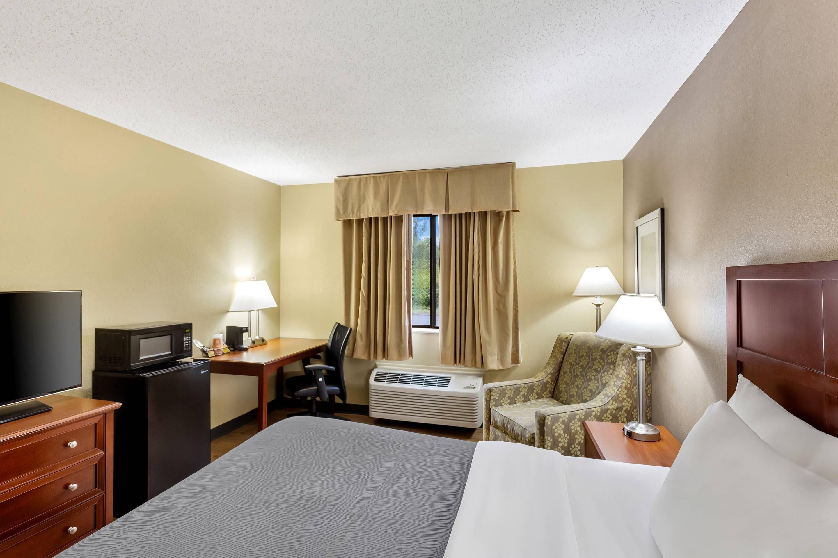 A hotel room with a bed, a desk, a television, a chair, and a window with curtains.