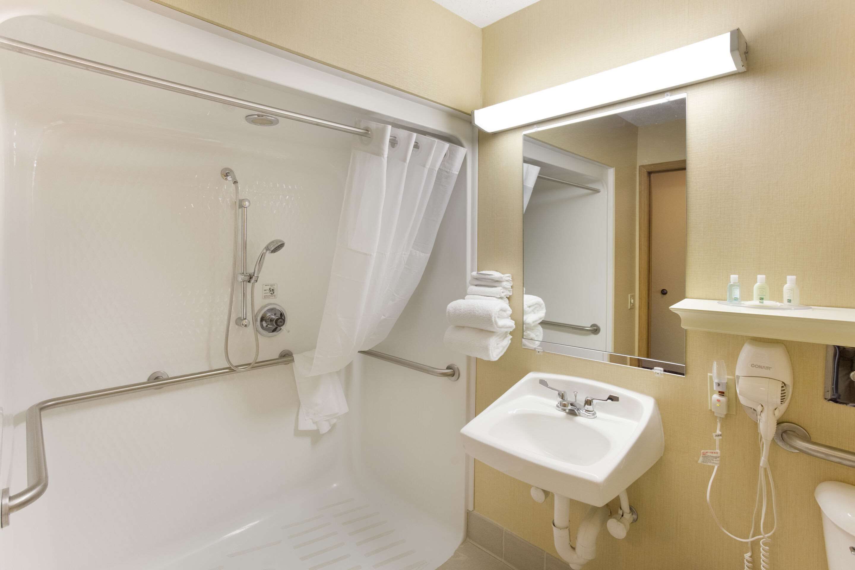 A bathroom with a shower, a sink, a mirror, and a towel rack.