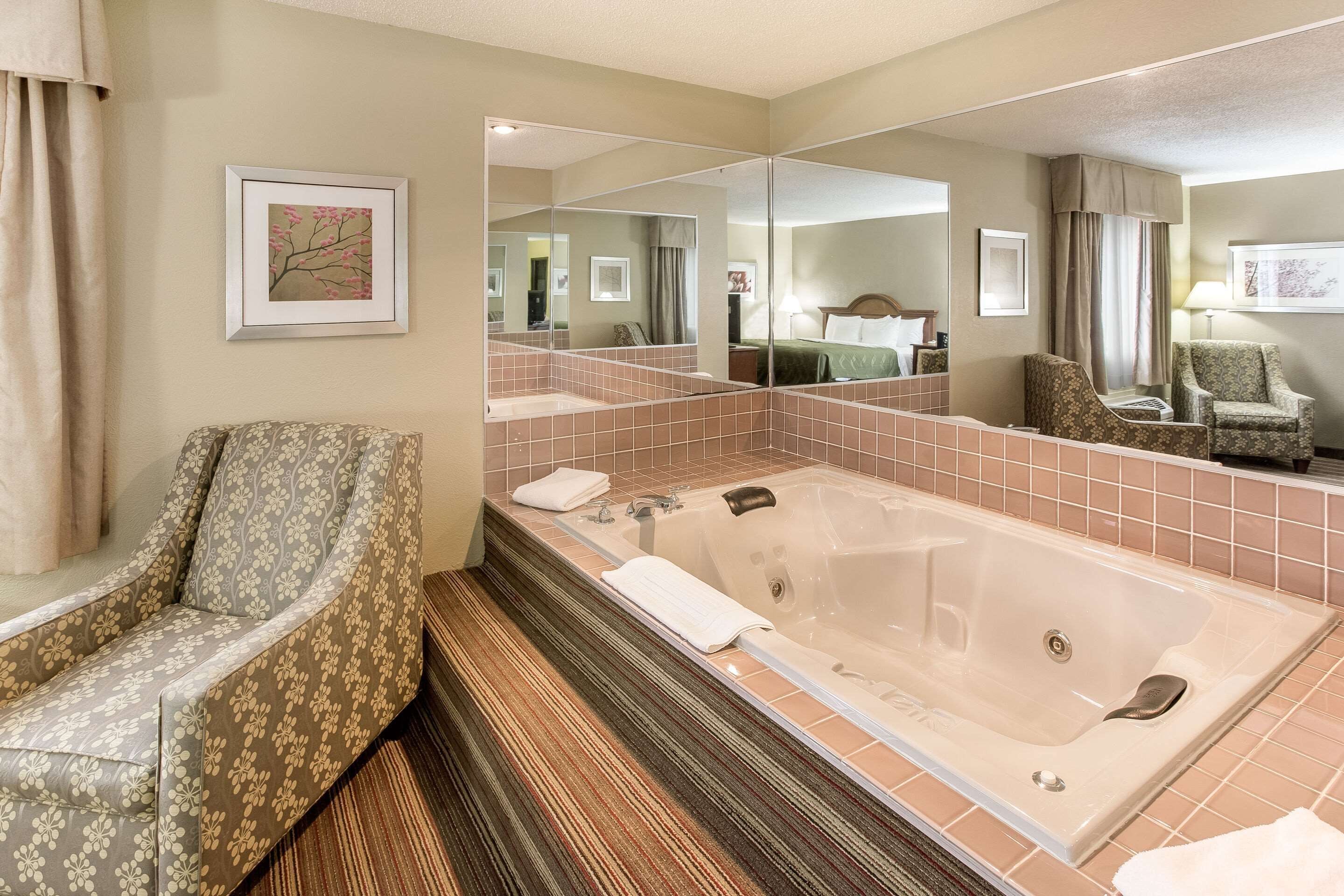 A bathroom with a large mirror, a bathtub, a chair, and a wooden floor.