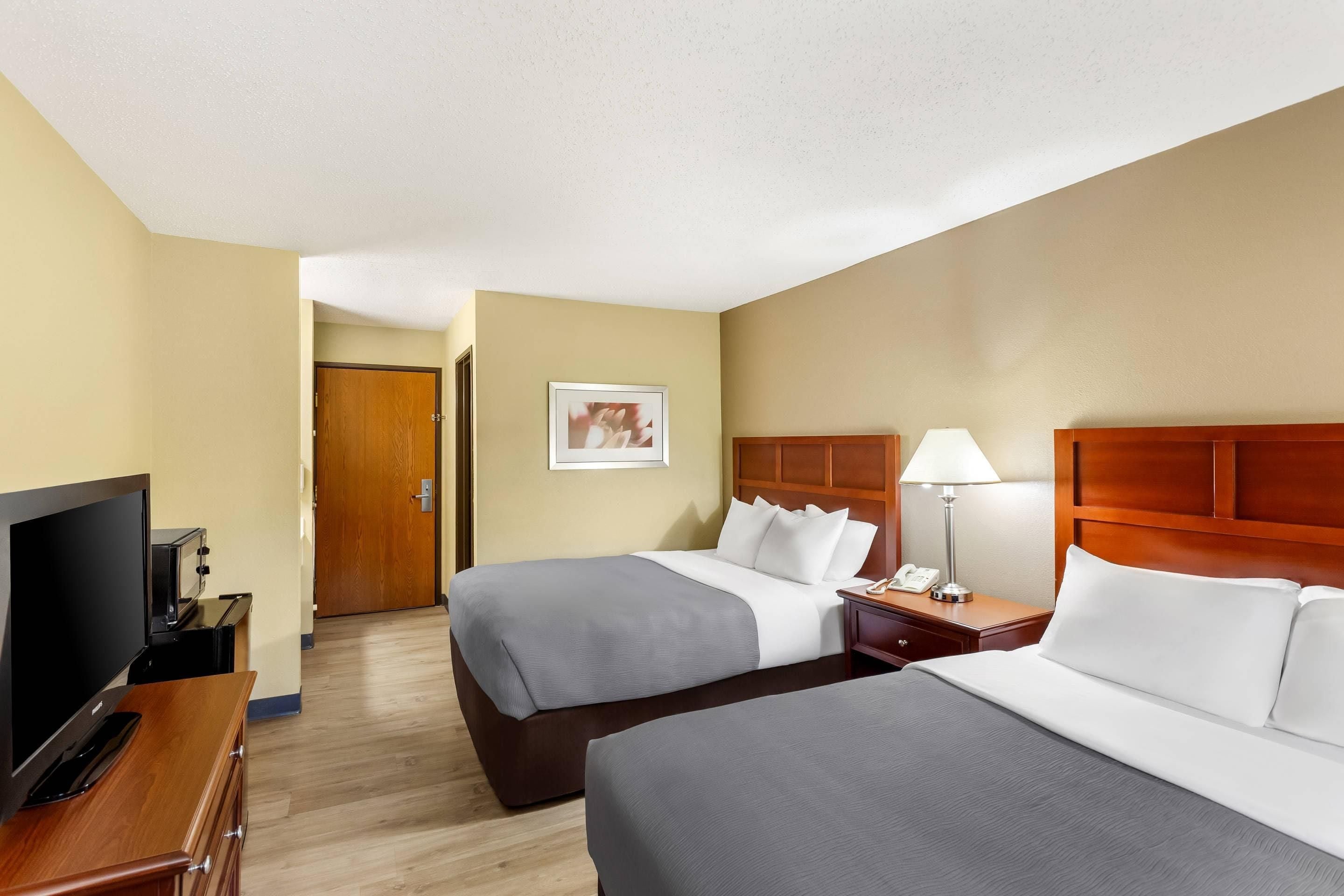 A hotel room with two beds, a TV, a desk, and a lamp.