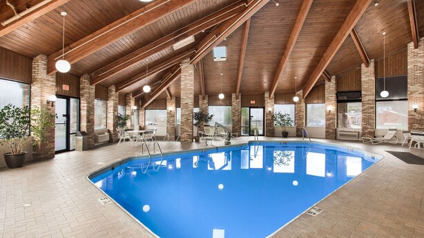 An indoor swimming pool with a wooden ceiling and brick walls, surrounded by lounge chairs and potted plants. - Quality Inn Athens (Athens)