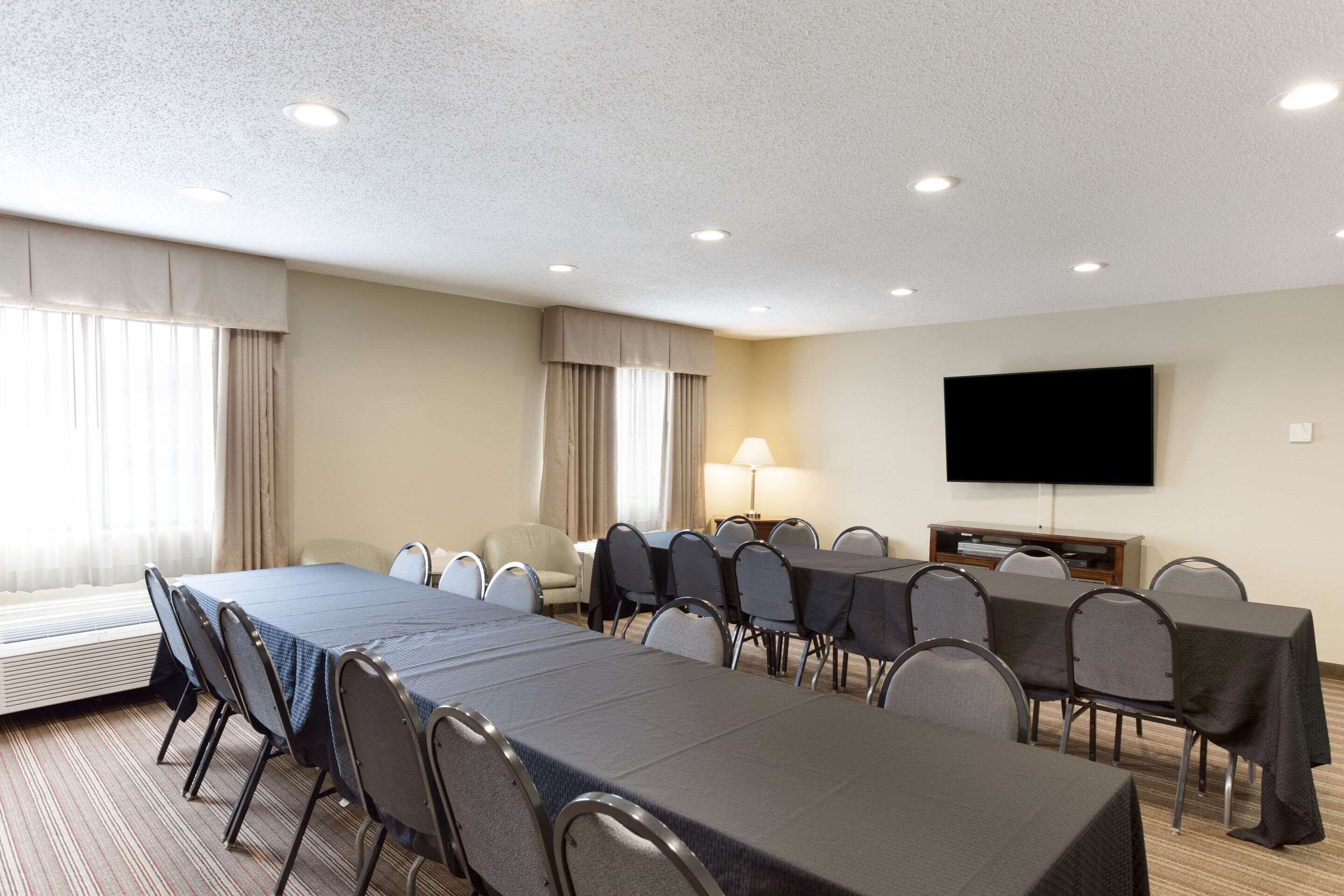 Une salle de conférence d’hôtel avec une longue table, des chaises, un téléviseur et une lampe.
