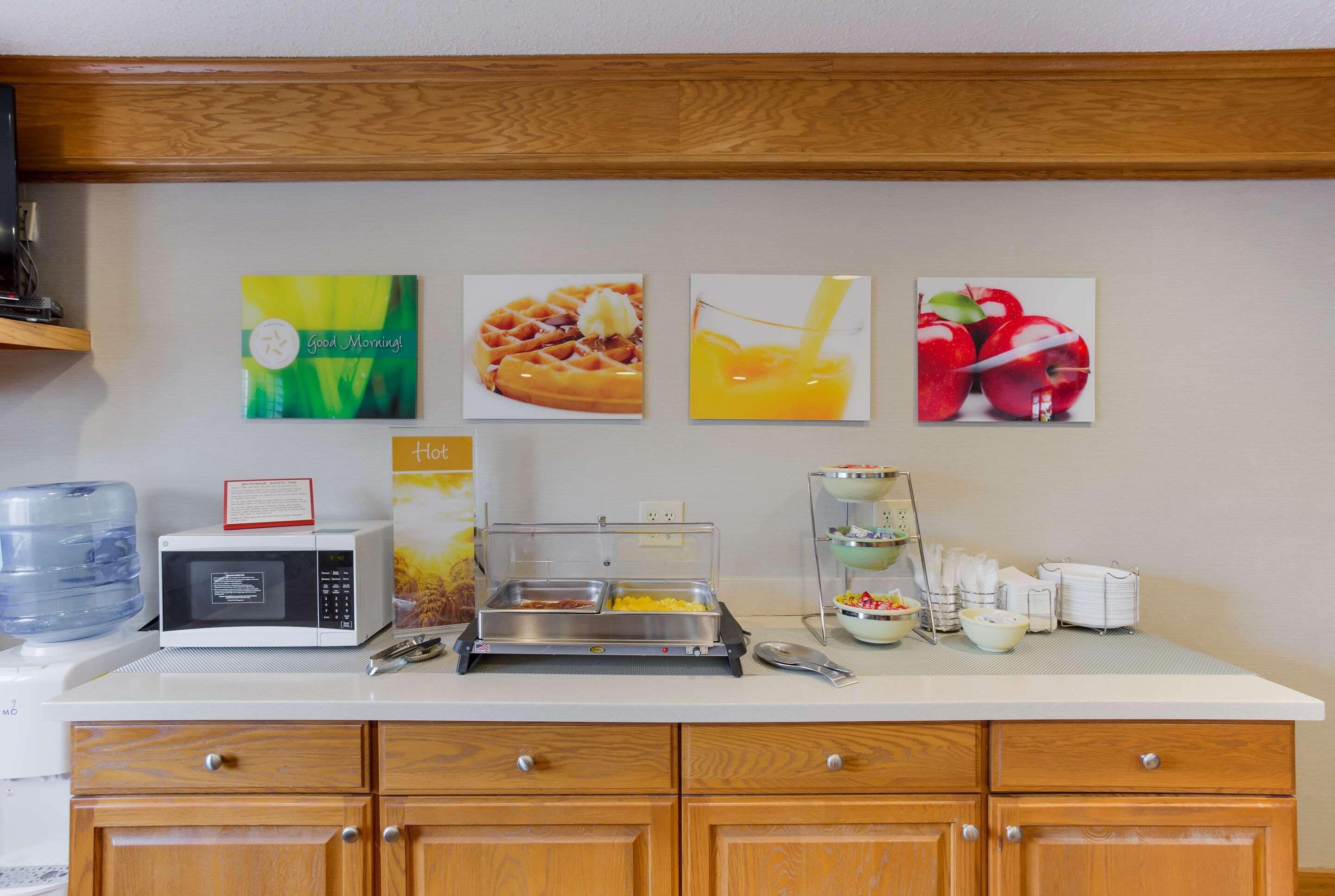 A breakfast bar with a microwave, waffle maker, and fruit display.