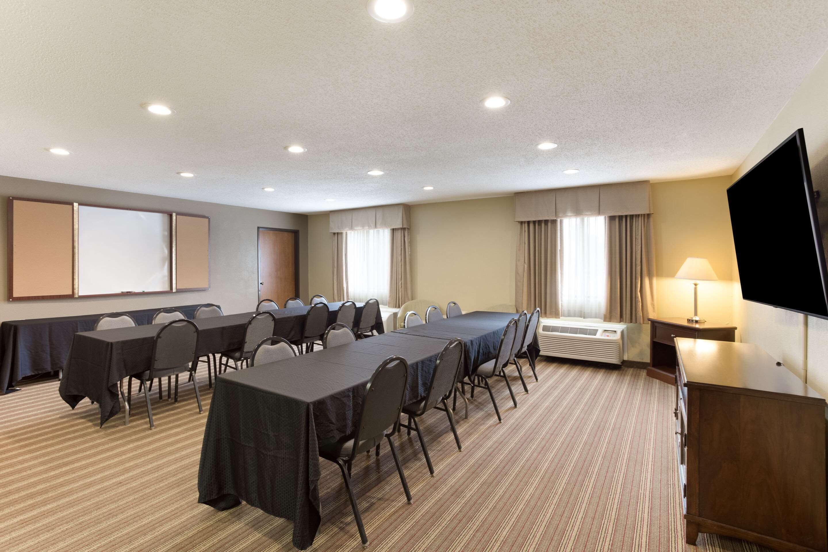A conference room with a long table, chairs, a projector screen, and a TV.