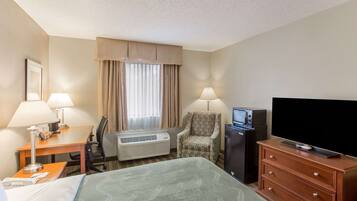 A hotel room with a bed, desk, chair, television, dresser, and air conditioning unit.