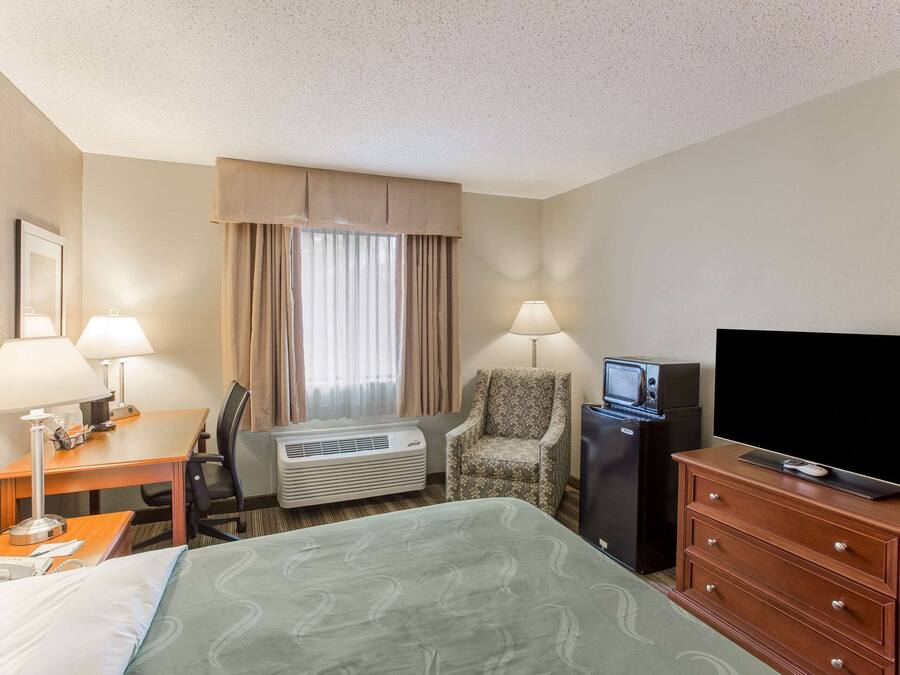 A hotel room with a bed, desk, chair, television, dresser, and air conditioning unit.