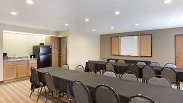 A conference room with a long table, chairs, a refrigerator, a coffee maker, and a whiteboard.