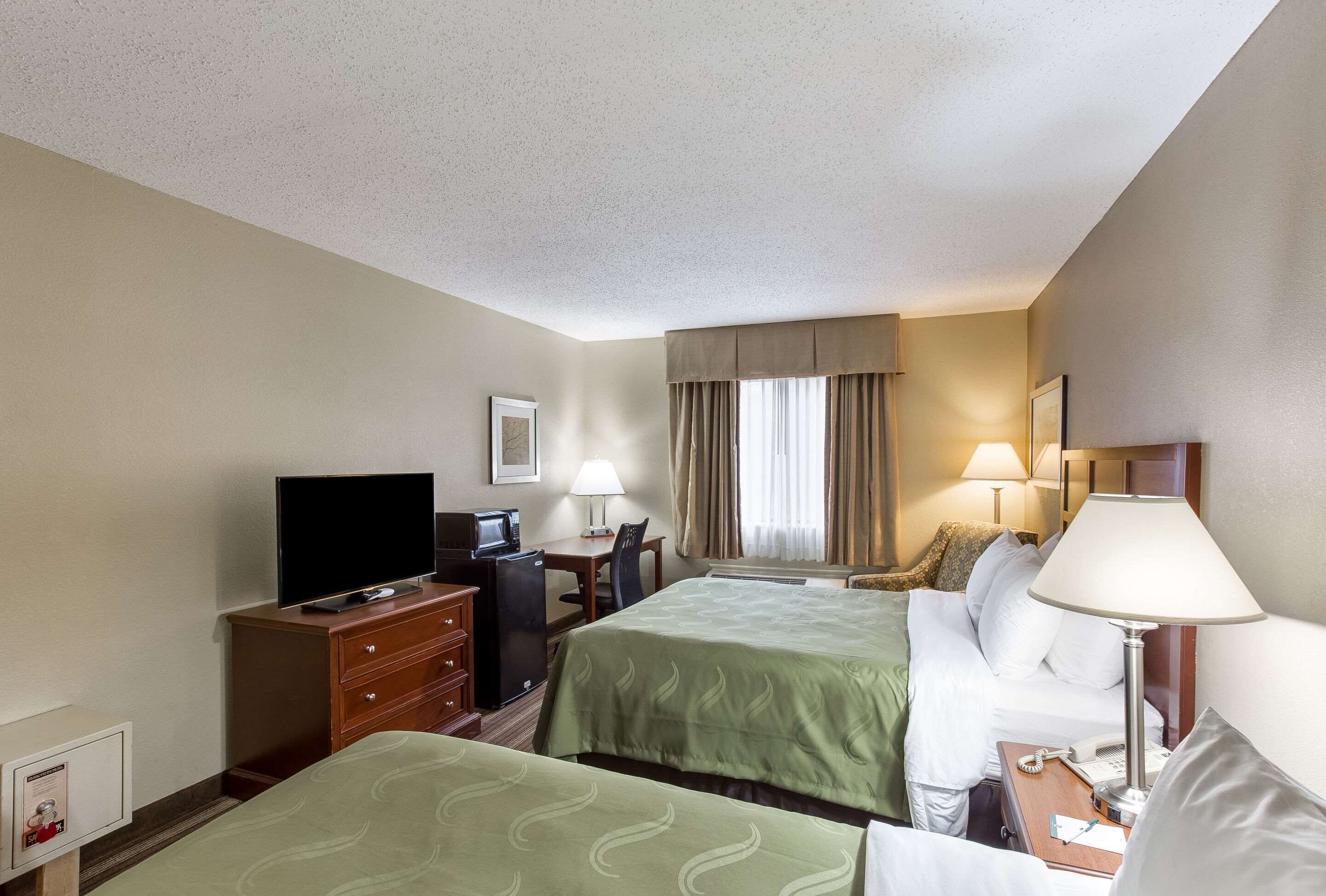 Habitación de hotel con dos camas, un escritorio con ordenador, televisión y un mueble pequeño.