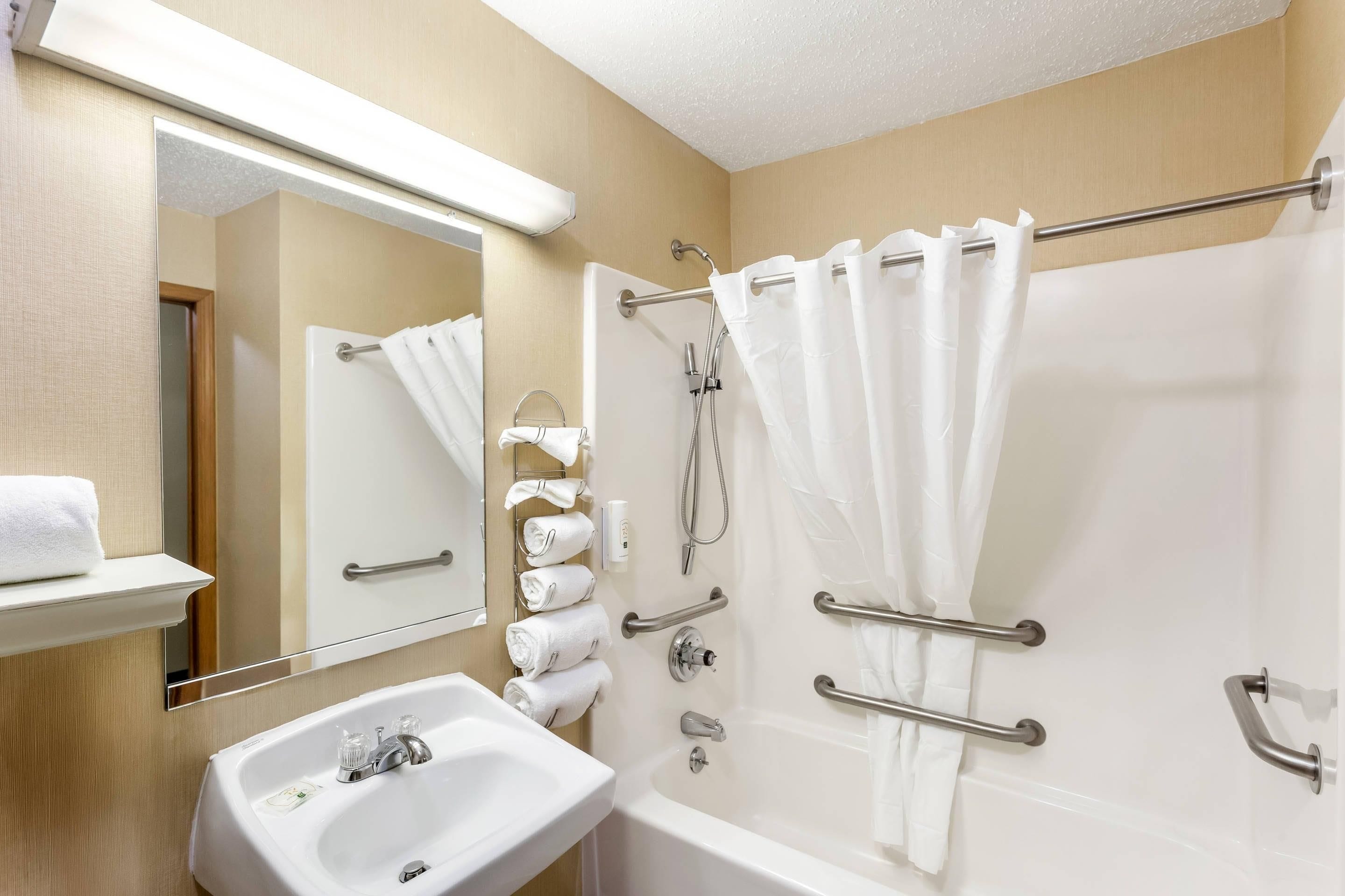A bathroom with a sink, mirror, towel rack, shower, and grab bars.