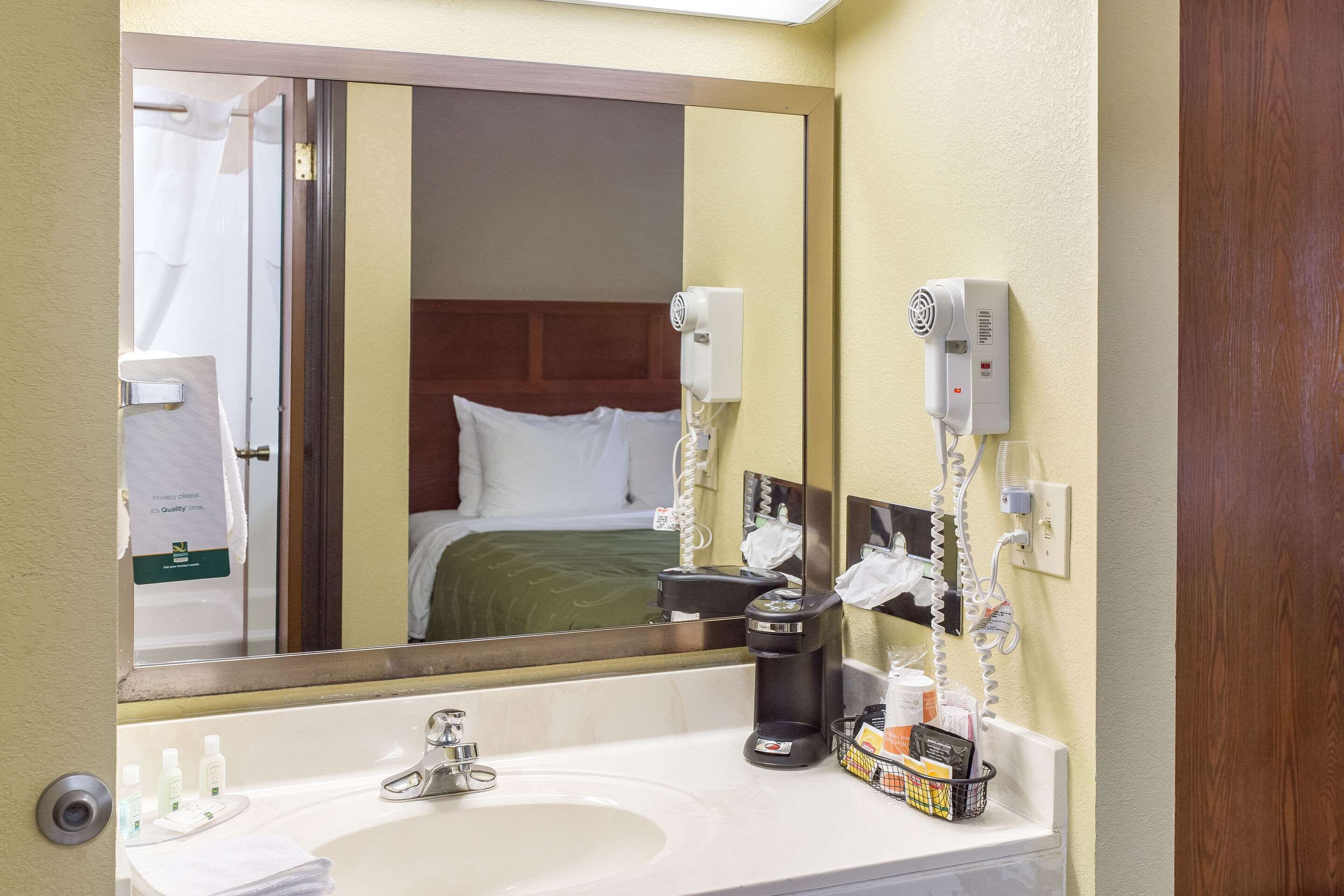 A hotel bathroom with a sink, mirror, hairdryer, and a coffee maker.
