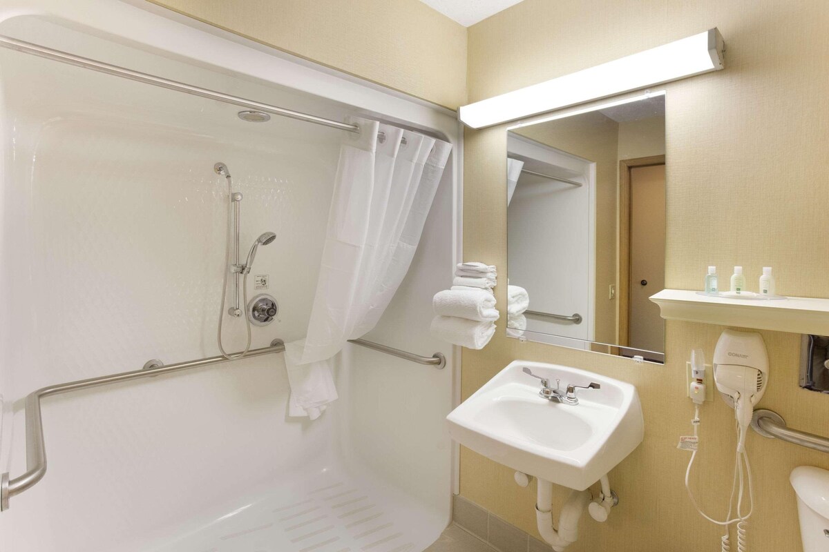 A bathroom with a shower, a sink, a mirror, and a towel rack.