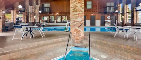An indoor swimming pool with multiple lanes, surrounded by lounge chairs and tables, and wooden paneling on the walls.