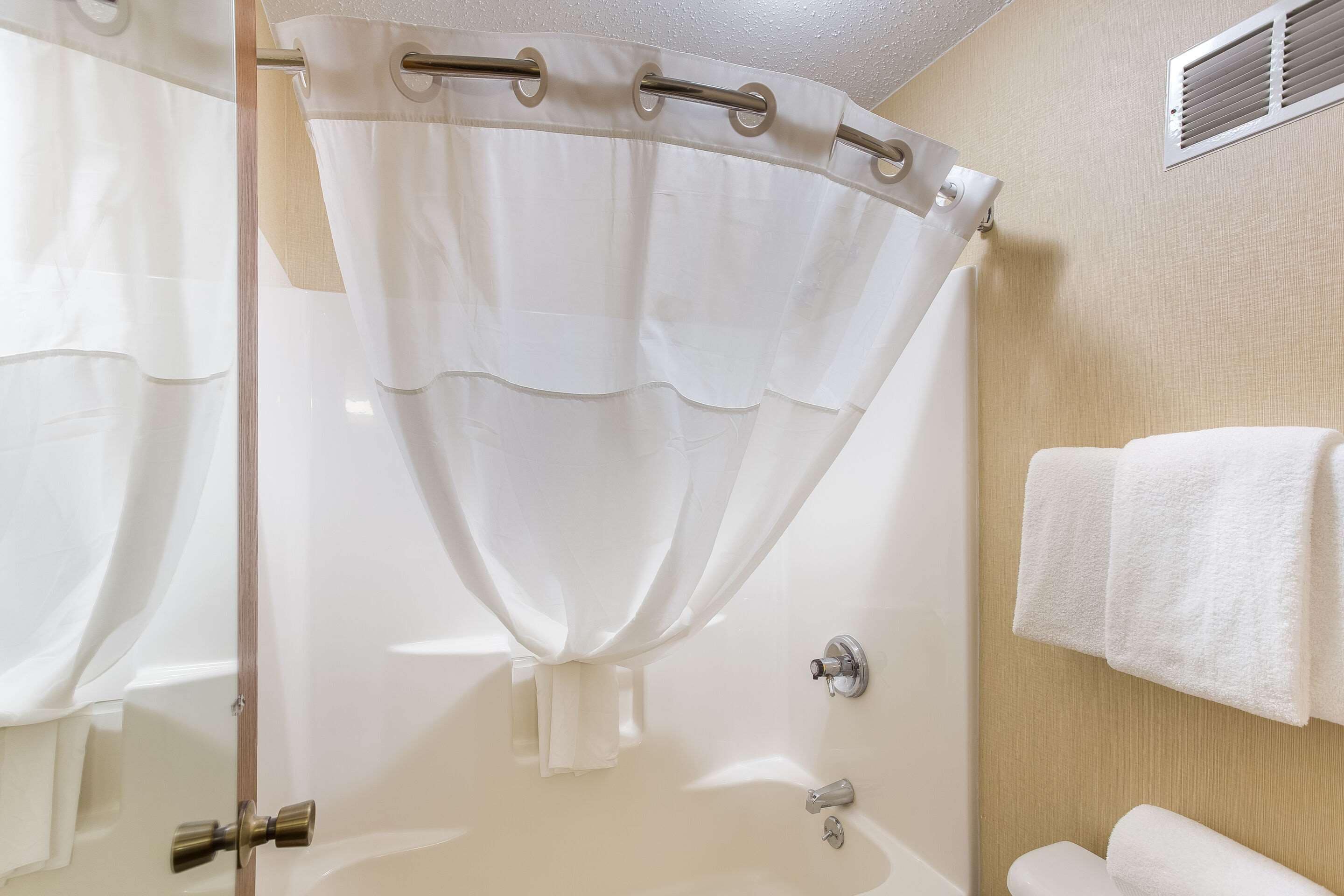A bathroom with a glass shower enclosure, a white bathtub, a towel rack with towels, and a visible toilet.