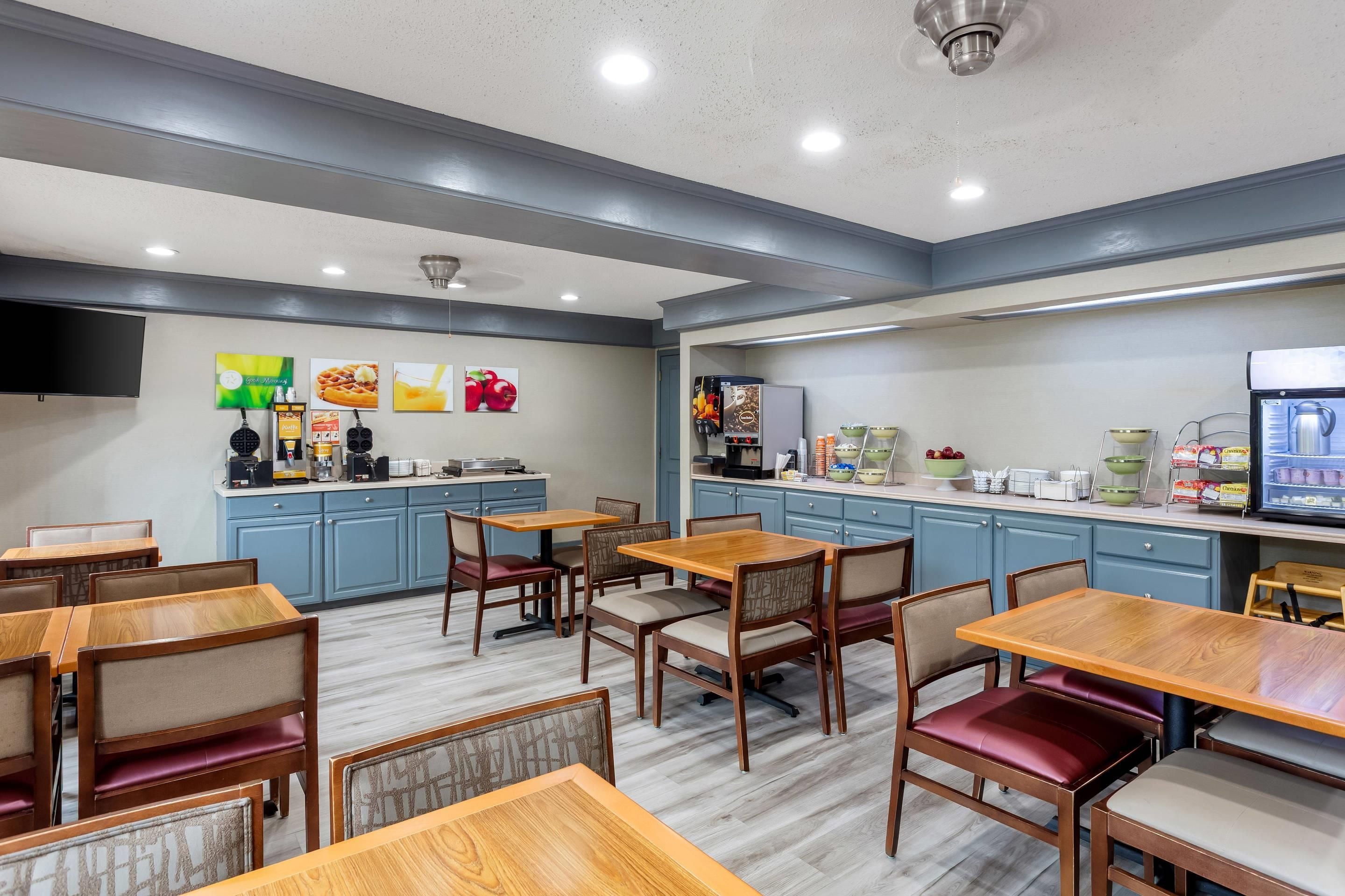 A restaurant with wooden tables and chairs, a coffee station, and a refrigerator.