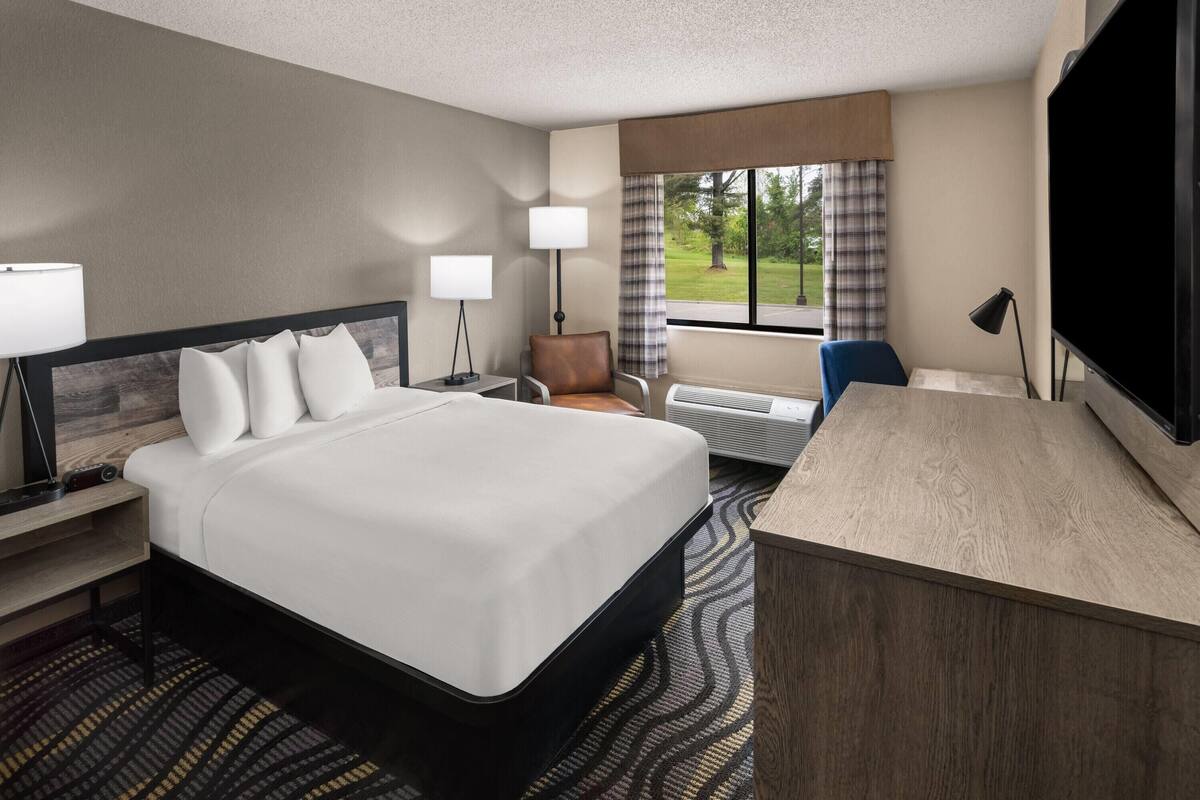 A hotel room with a large bed, a desk, a chair, a TV, and a window with curtains.