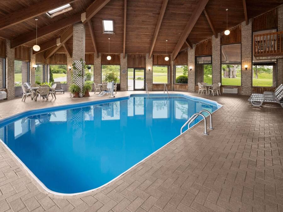 Une piscine intérieure dotée d’un sol en briques, de poutres en bois au plafond et d’espaces aménagés avec des chaises et des tables.