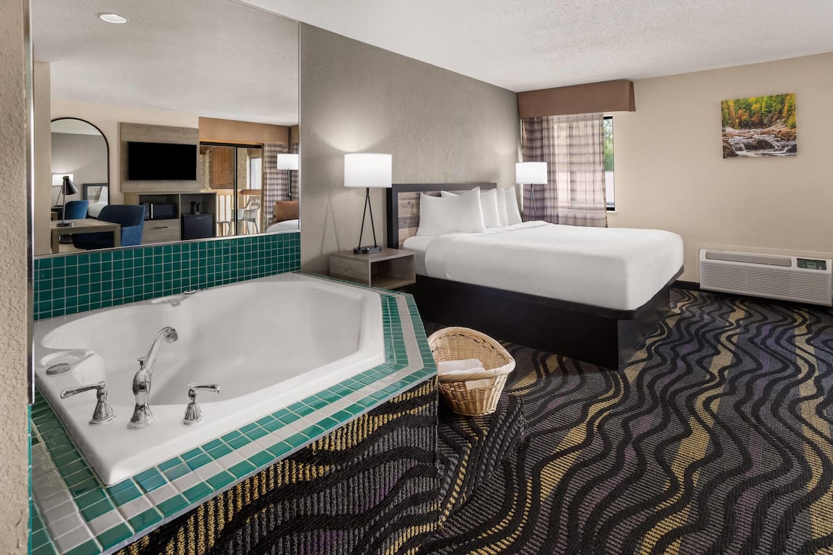 A hotel room with a large bathtub, two beds, a flat-screen TV, a desk with a chair, and a large mirror.
