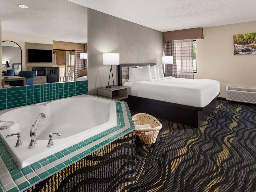 A hotel room with a large bathtub, two beds, a flat-screen TV, a desk with a chair, and a large mirror.
